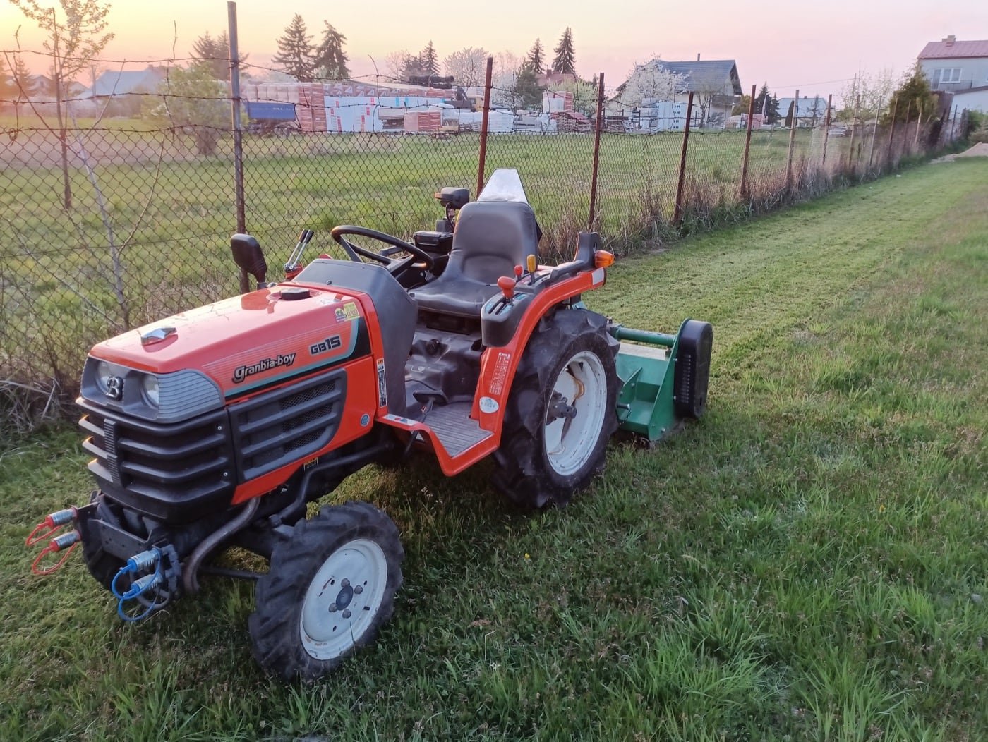 Ciągnik Kubota z kosiarką bijakową przy wykoszonym pasie działki